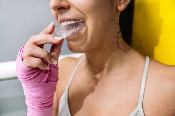 A woman with a bandaged hand is brushing her teeth with a toothbrush.