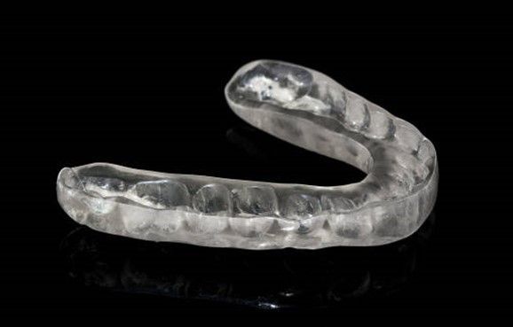 A clear mouth guard is sitting on a black surface.