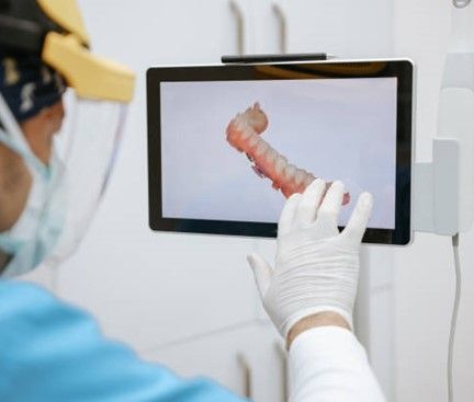 A dentist wearing a mask and gloves is touching a tablet screen.