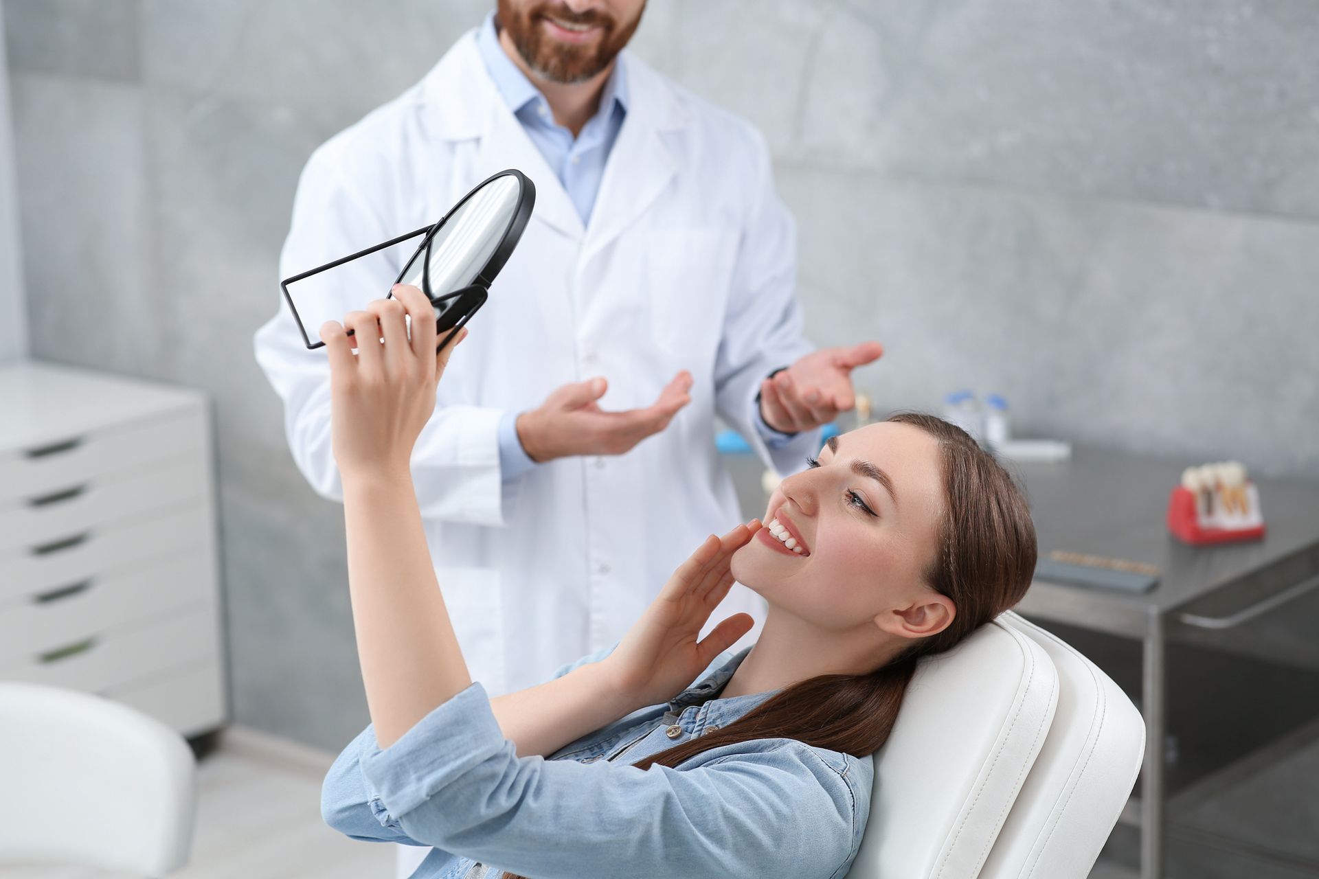 A woman next to a dentist smiling while looking at her all-on-four dental implants in the mirror.