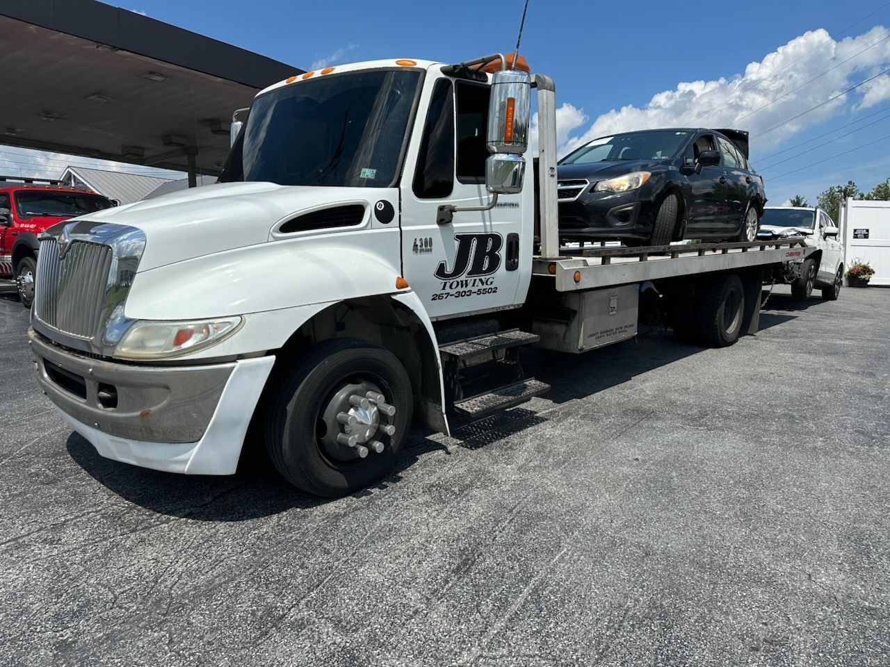 A white tow truck with two cars on the back is parked in a parking lot.