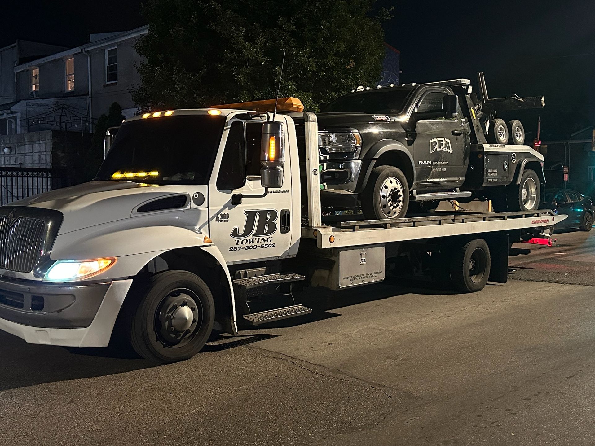 A tow truck with two cars on the back is parked on the side of the road at night.