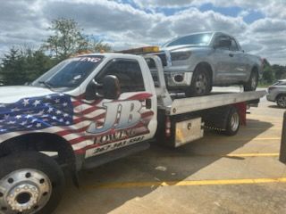 A tow truck with two cars on the back is parked in a parking lot.