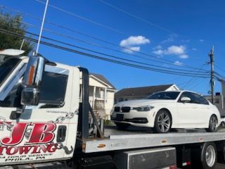 A white car is sitting on the back of a tow truck.
