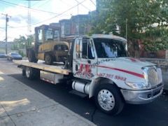 A tow truck with a forklift on the back is parked on the side of the road.