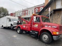 A red tow truck is towing a white truck down a street.