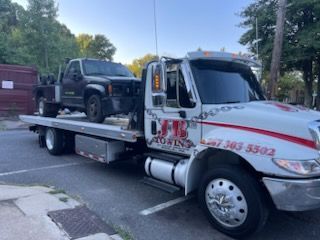 A tow truck is carrying a truck on the back of it.