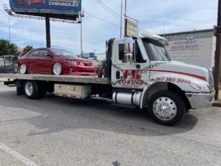 A tow truck with a red car on the back is parked in a parking lot.