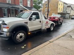 A white tow truck is towing a red car down a street.