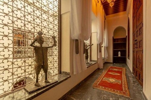 Narrow hallway with patterned rug, decorative metal window, statue, and arched doorway.