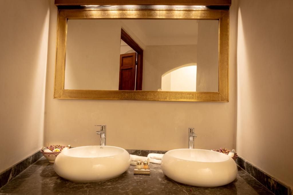 Double sink bathroom with gold-framed mirror, white sinks, and black countertop.