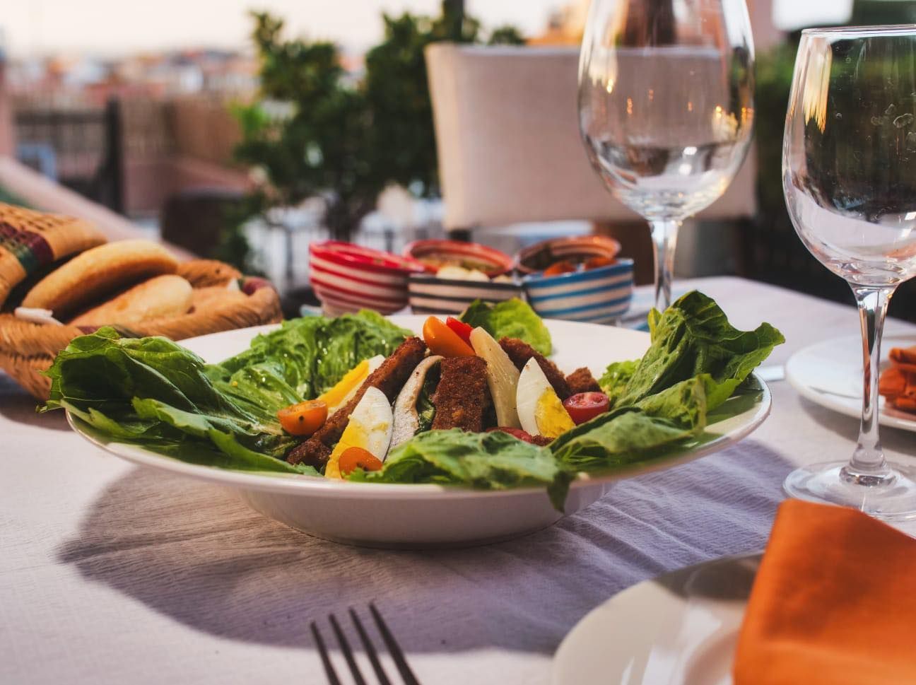 A white plate topped with a salad and a glass of wine on a table.