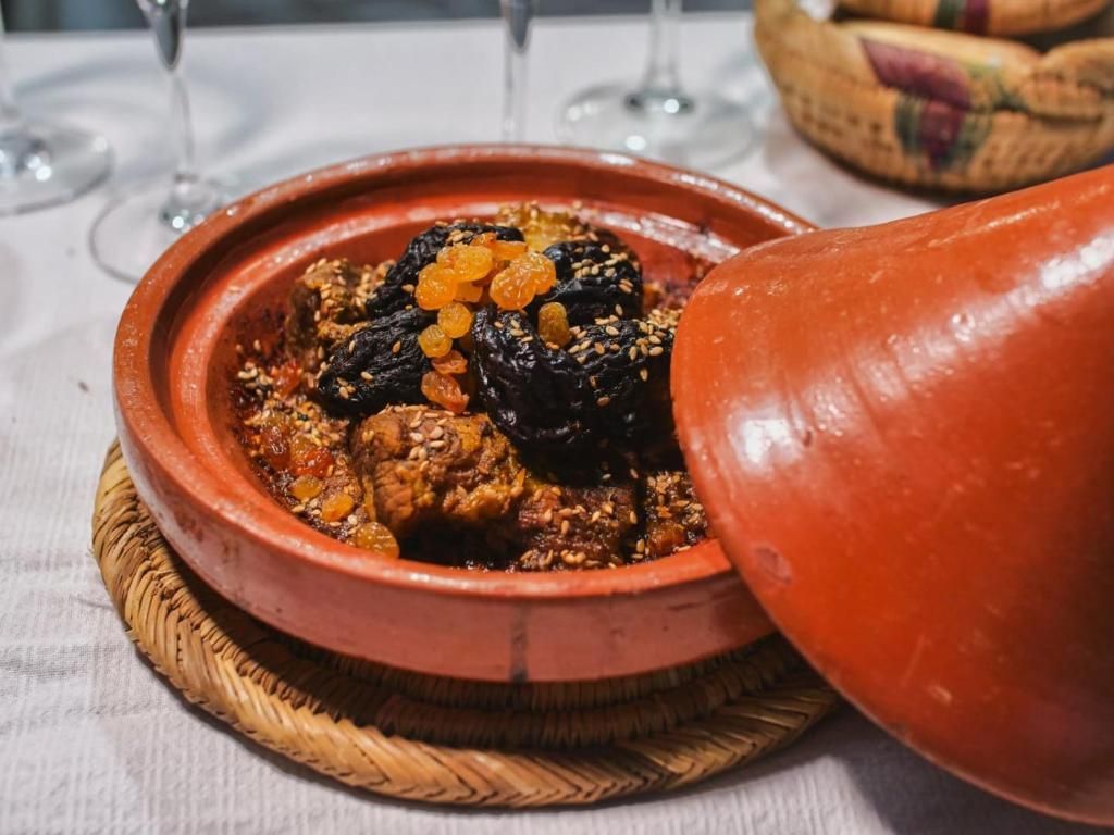 A clay pot filled with meat and raisins on a table.