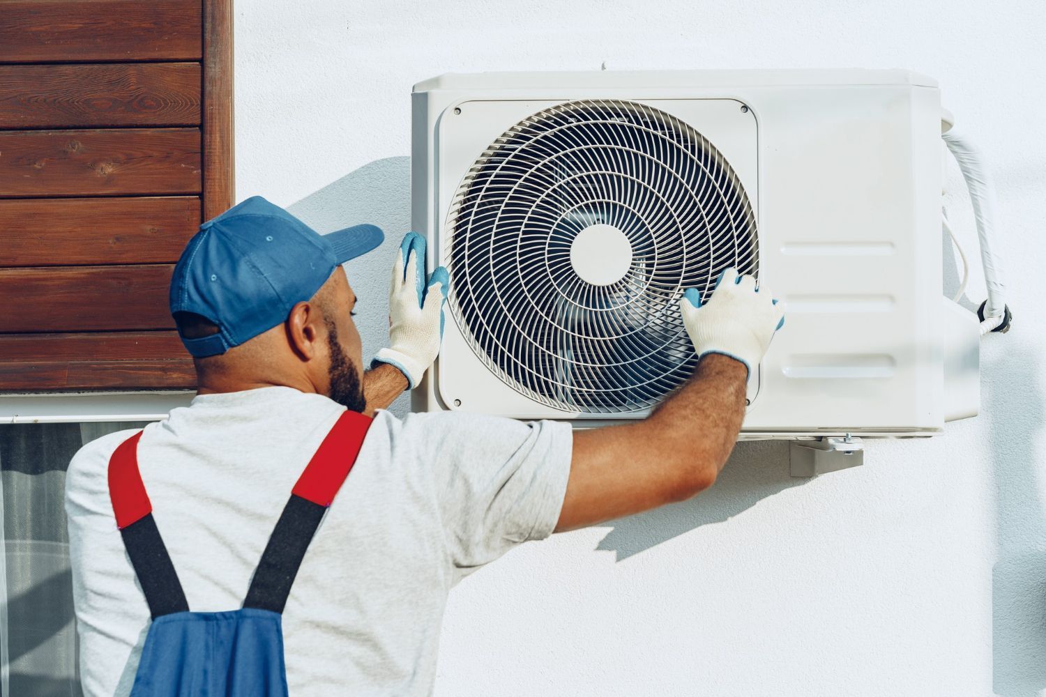 Man in overalls and gloves servicing an outdoor air conditioning unit.