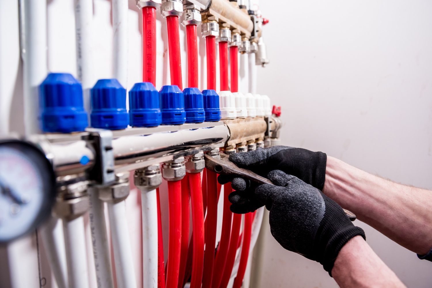 Person wearing gloves working on red and white pipes connected to a manifold with blue caps.