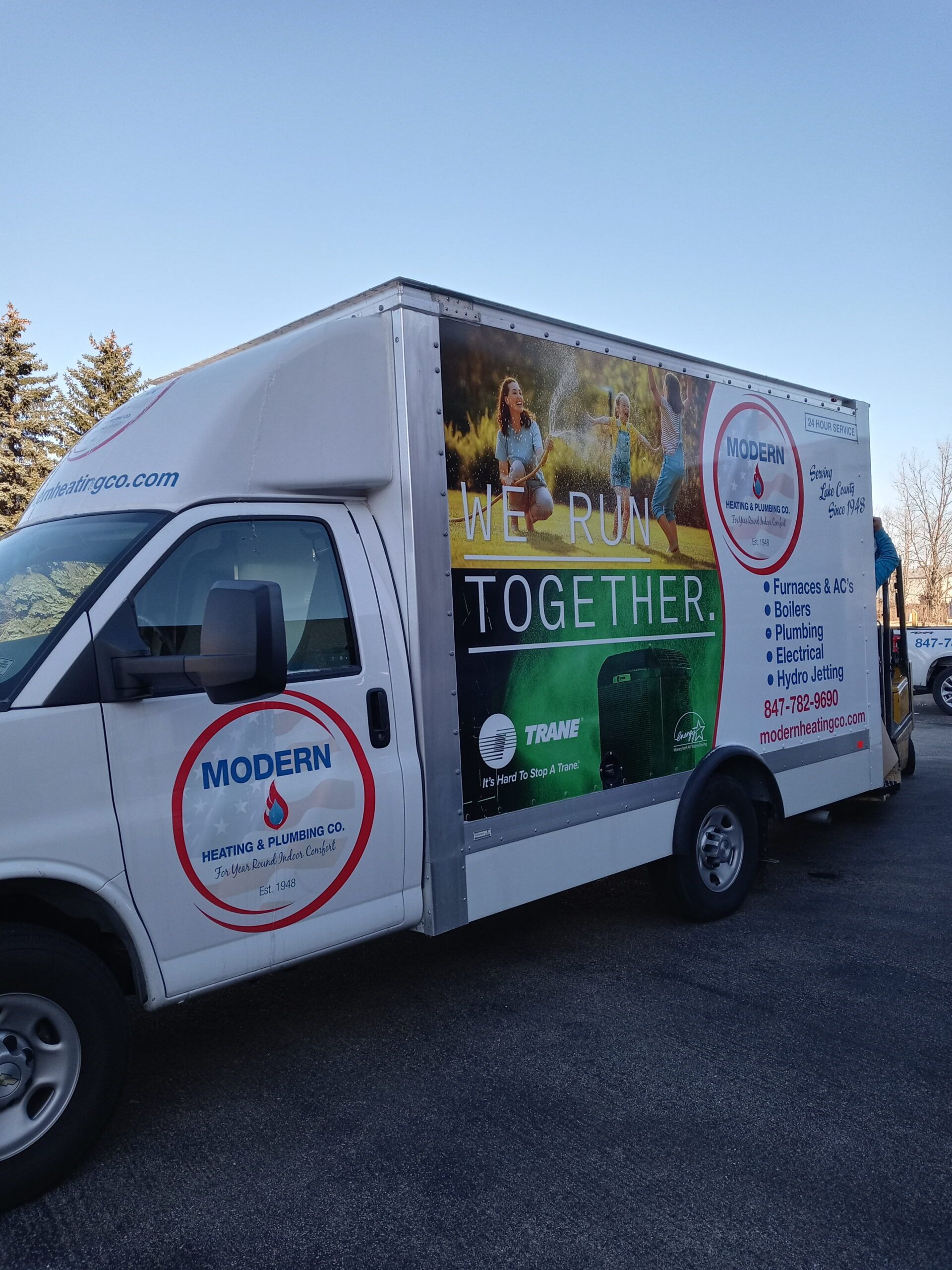 White work van with logo, parked outside. Side displays a colorful advertisement with people.