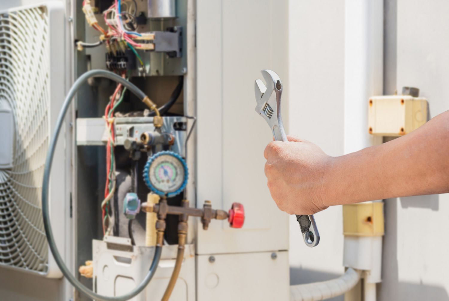 Hand holding a wrench, repairing an air conditioning unit outdoors.