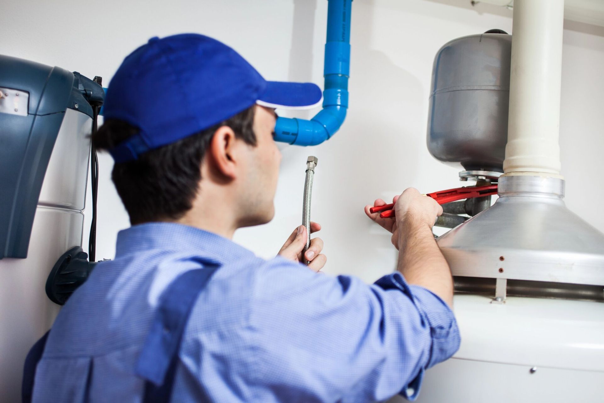 Plumber in blue uniform working on a water heater, using a wrench indoors.