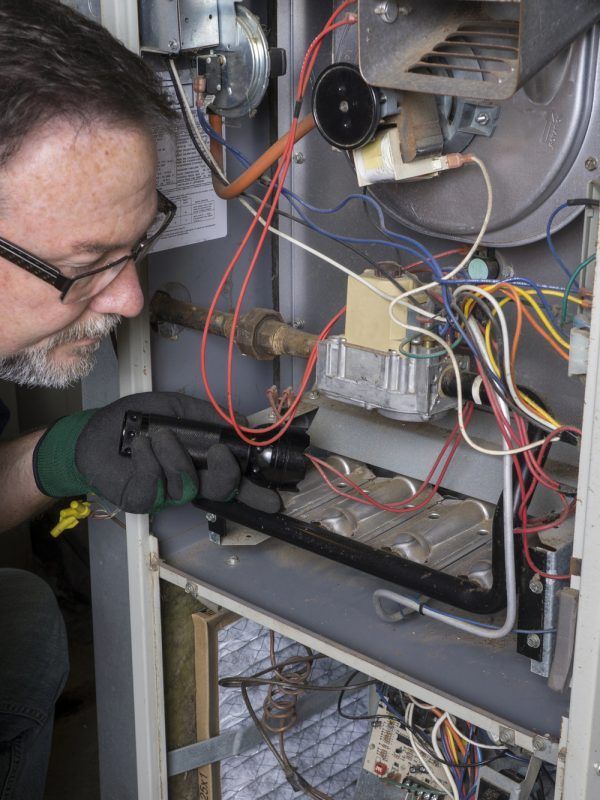 Man in glasses inspecting a furnace with a flashlight.
