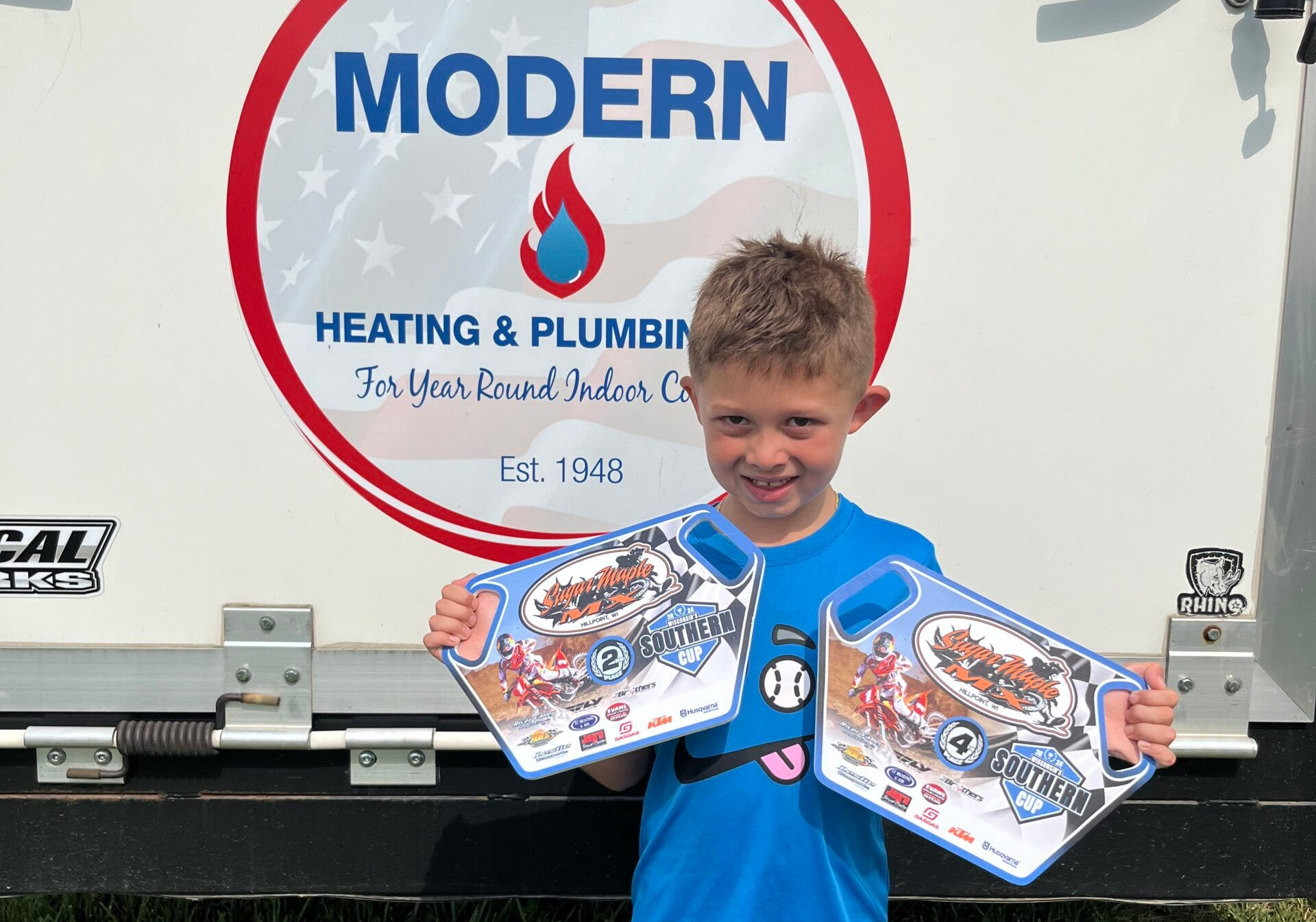 Boy holding two promotional signs in front of a Modern Heating & Plumbing truck.
