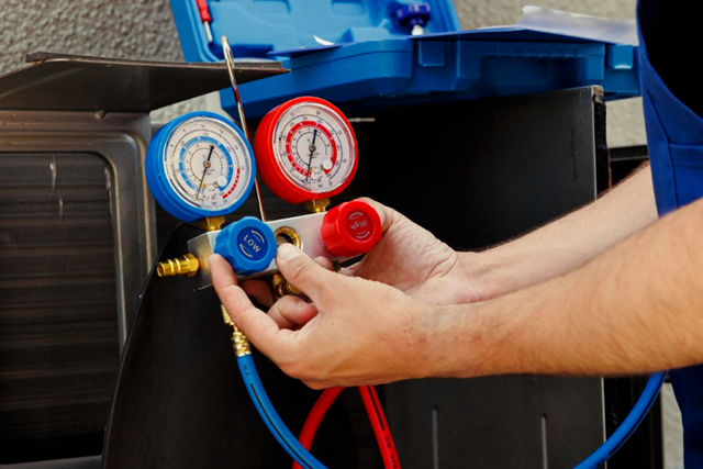 Person adjusts gauges on an air conditioning unit. Blue and red gauges, blue and red hoses.