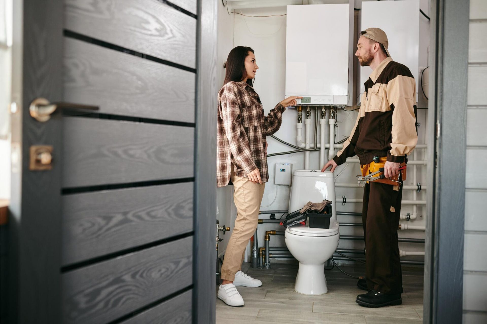 Woman and worker talking near a toilet and water heater in a utility room.