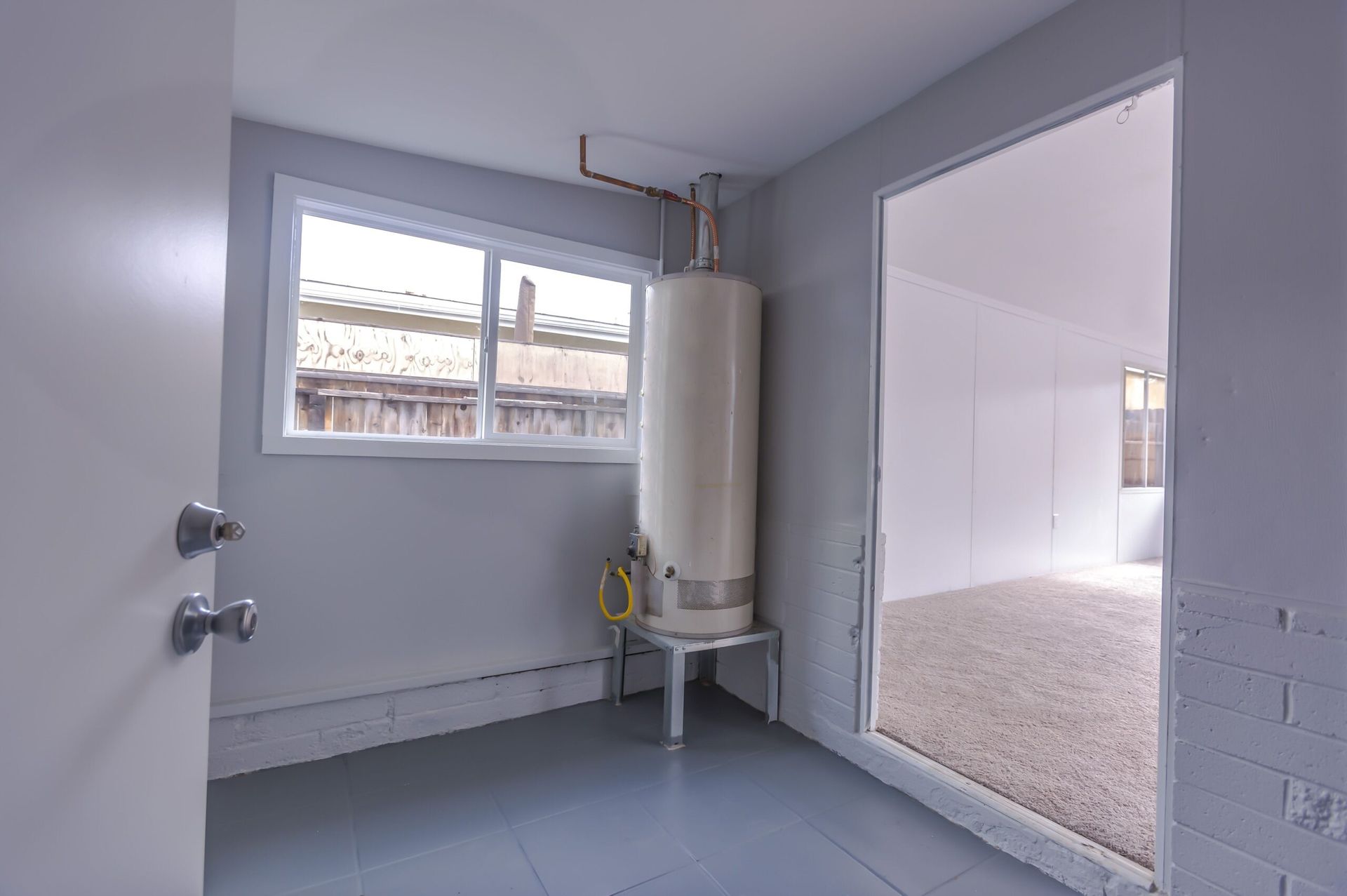 Interior view: Water heater near a window, doorway to a room with light-colored flooring.