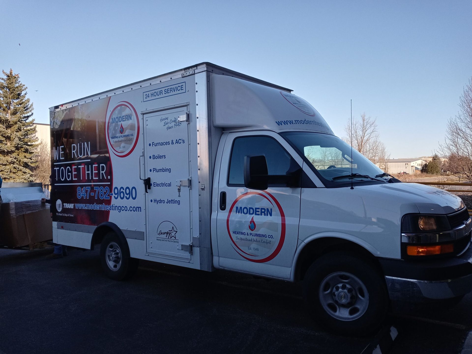 White box truck with company logos and phone number parked outdoors.