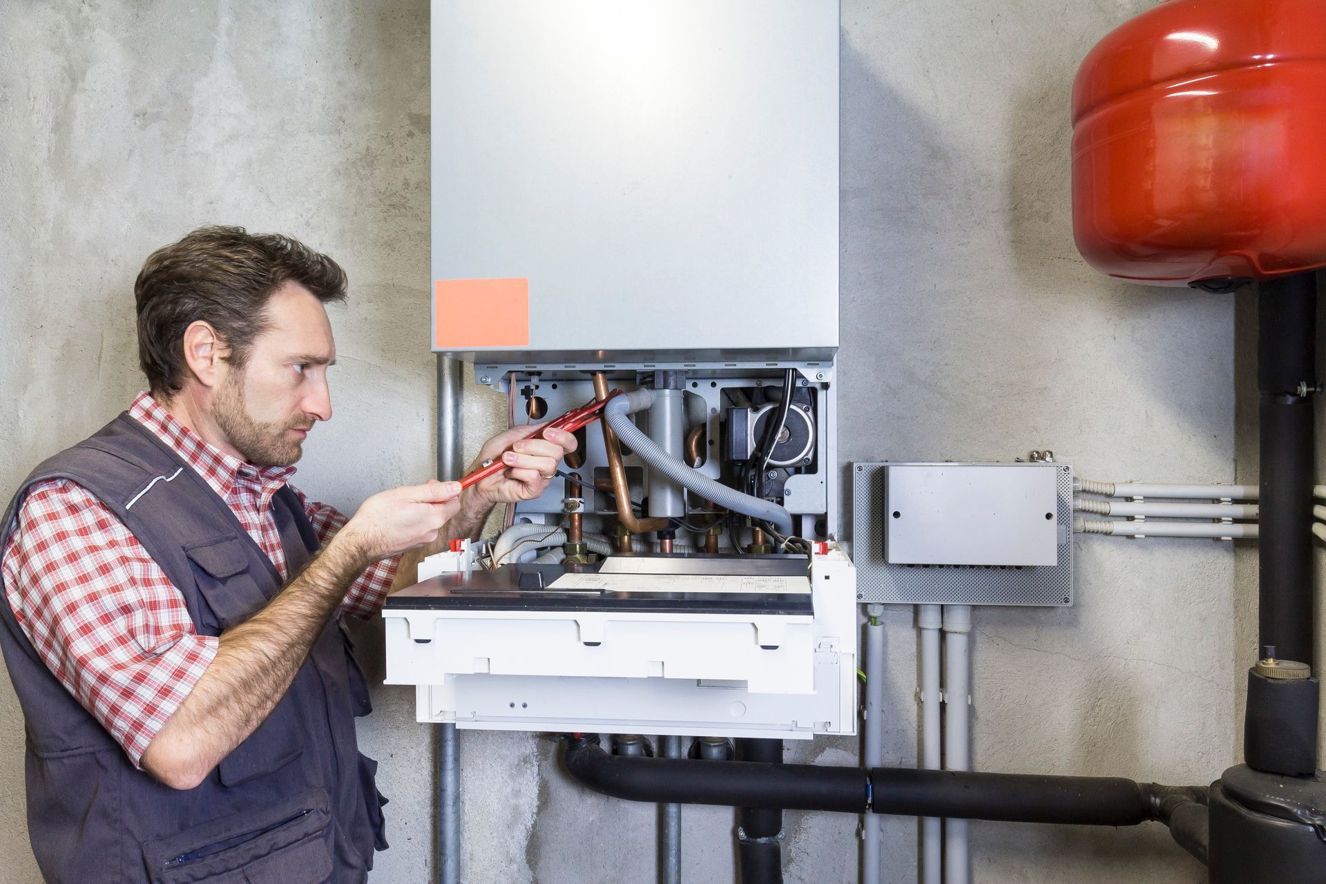 Man in work vest repairs a furnace with a tool in a utility room.