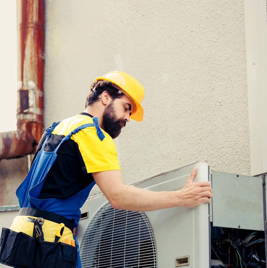 HVAC technician in yellow hard hat and blue overalls installs an air conditioning unit.
