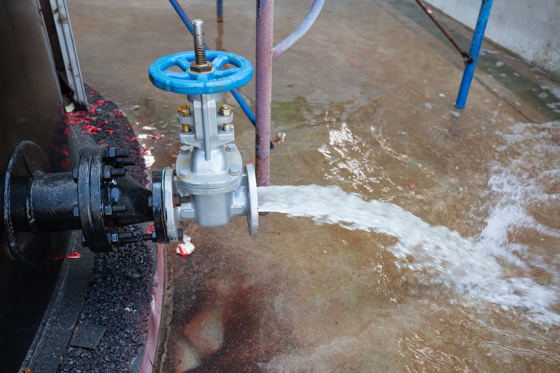 Valve with blue handle releasing a stream of water onto a concrete floor.