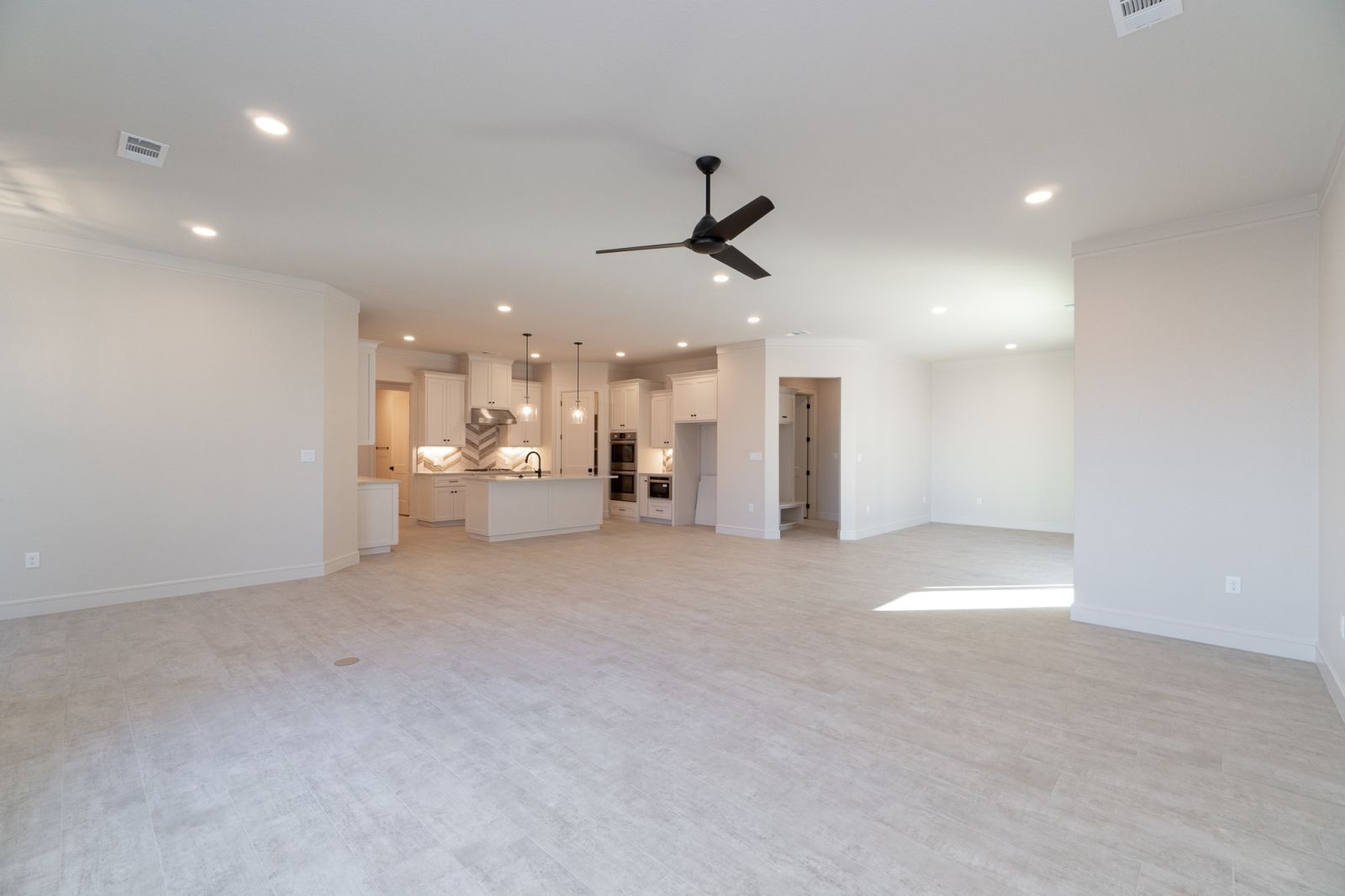 An empty room with a ceiling fan and a kitchen in the background