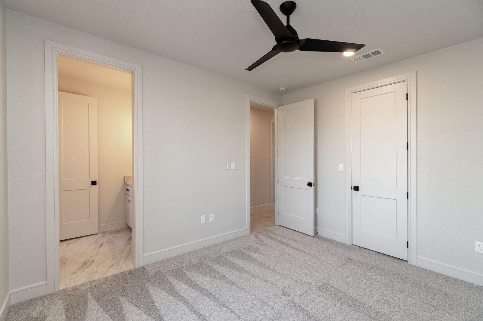 An empty bedroom with a ceiling fan and a bathroom in the background.