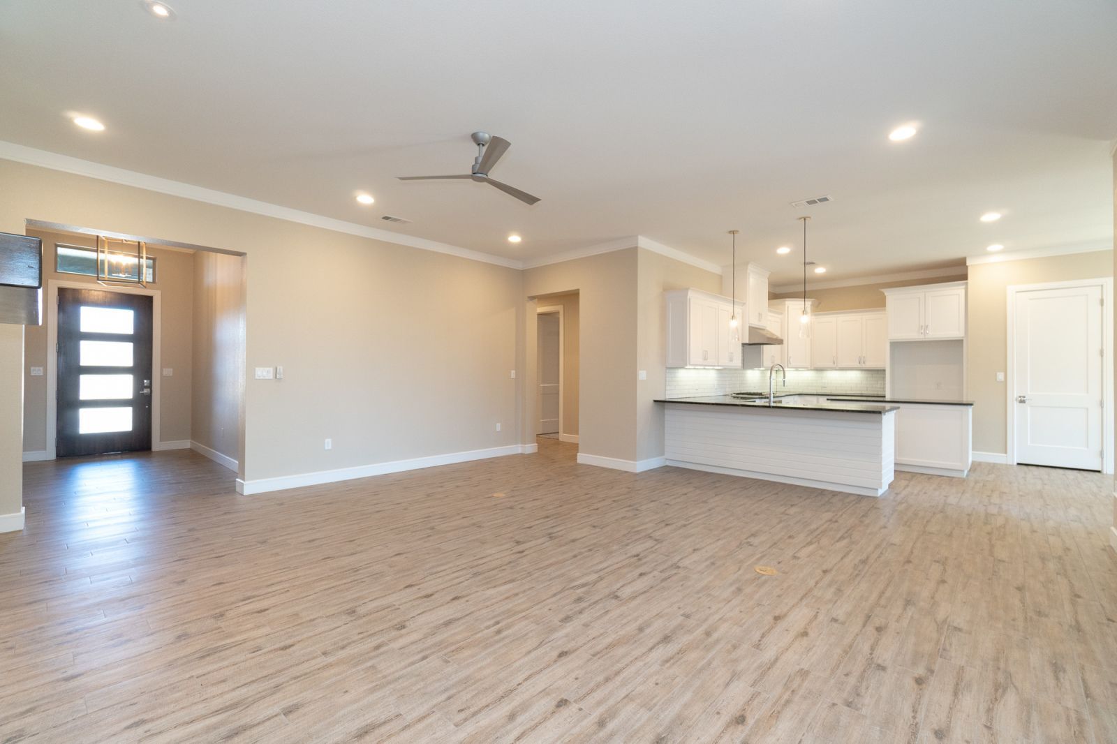 A living room with a ceiling fan and a kitchen in the background