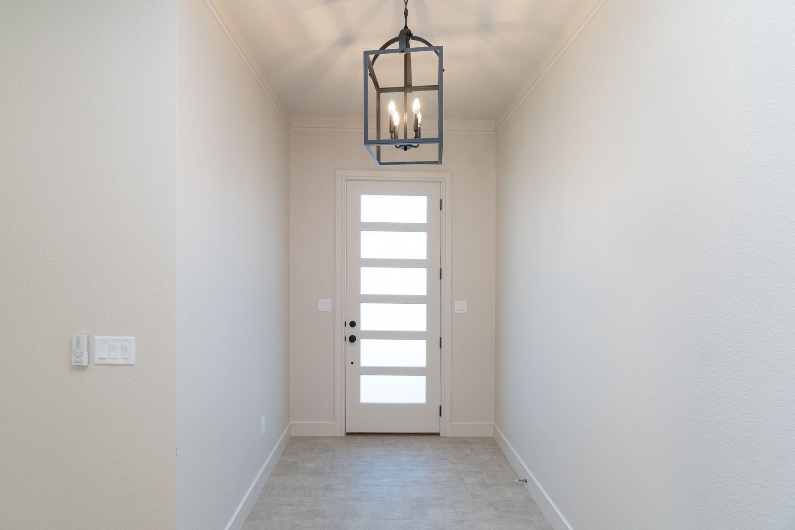 A hallway with a white door and a chandelier hanging from the ceiling