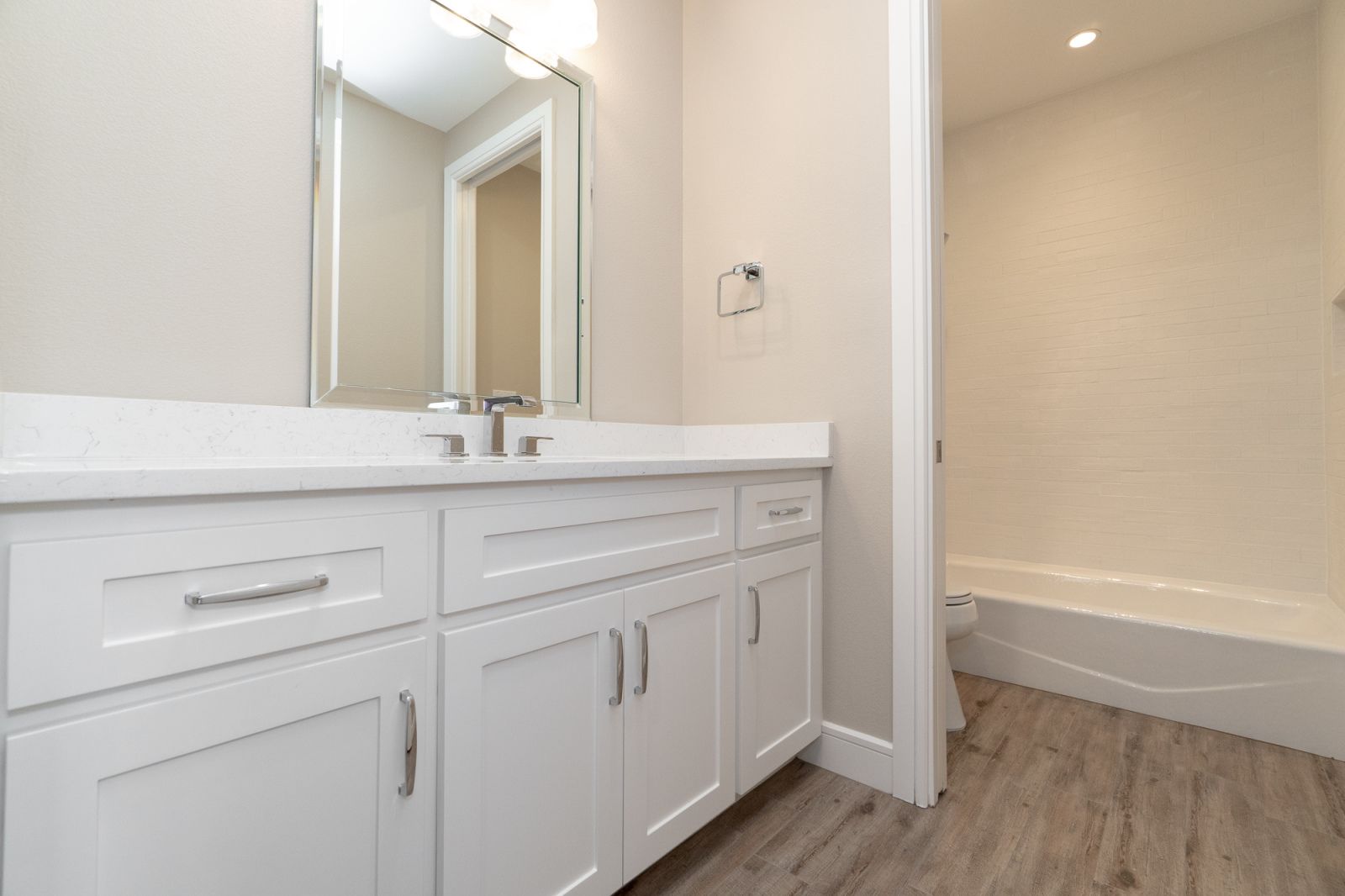 A bathroom with white cabinets , a sink , a mirror and a tub.