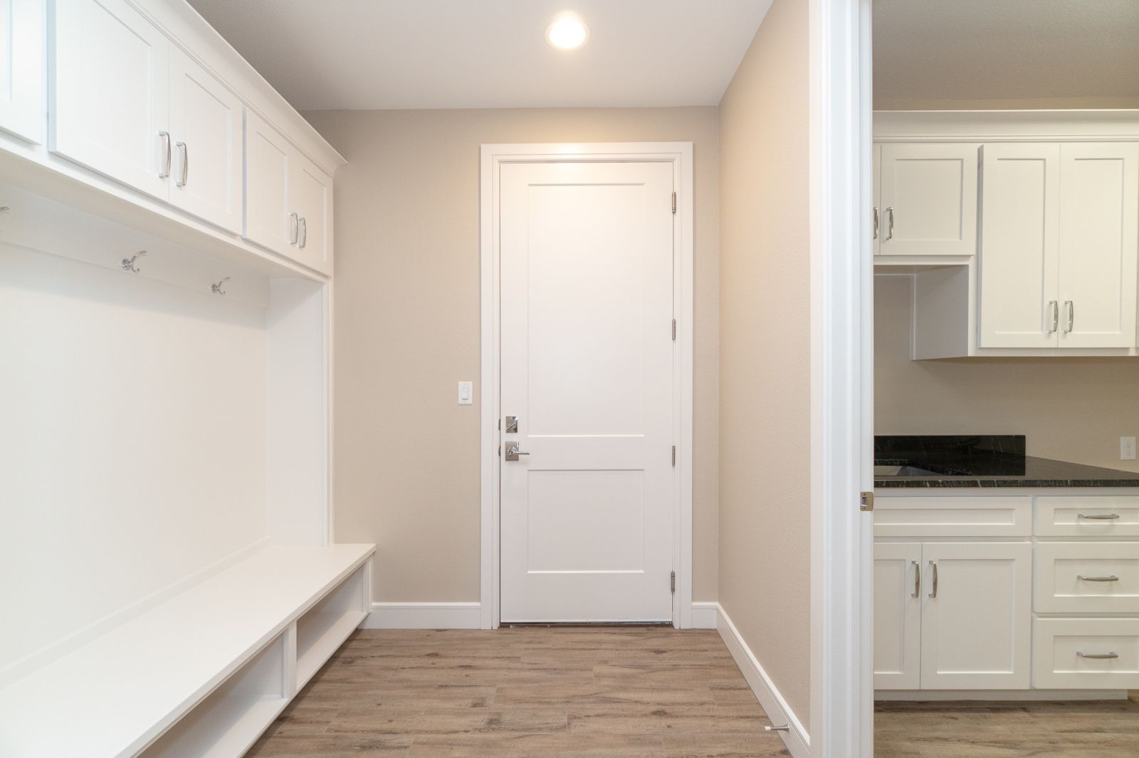 A hallway with white cabinets and a white door leading to a kitchen.