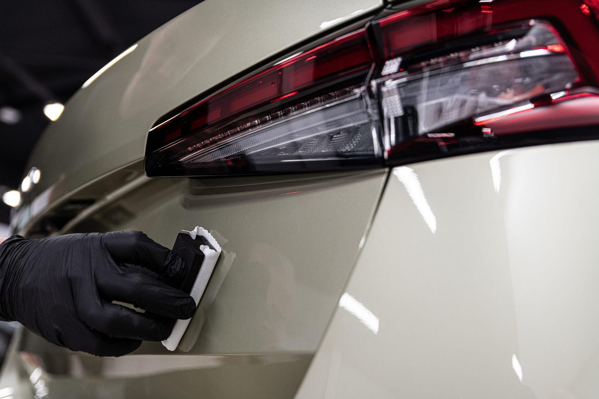 Person in black gloves applying ceramic coating to white car.
