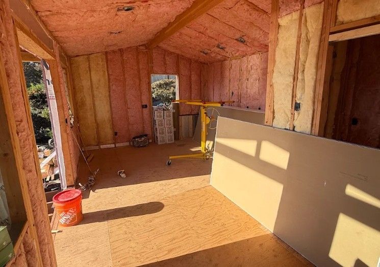 Interior of a room under construction with pink insulation. Drywall leans against a wall.