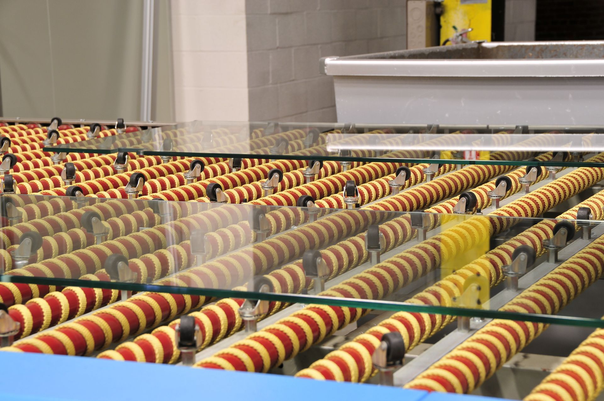 Glass sheets moving along a conveyor belt with red and yellow rollers in a factory setting.