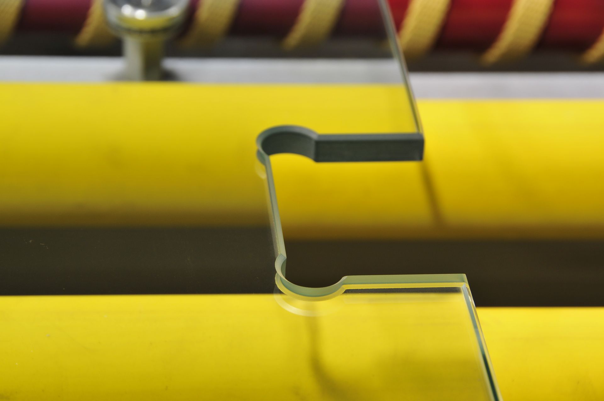Close-up of a yellow and gray metal piece being bent by a machine, with yellow and red cylindrical bars in the background.