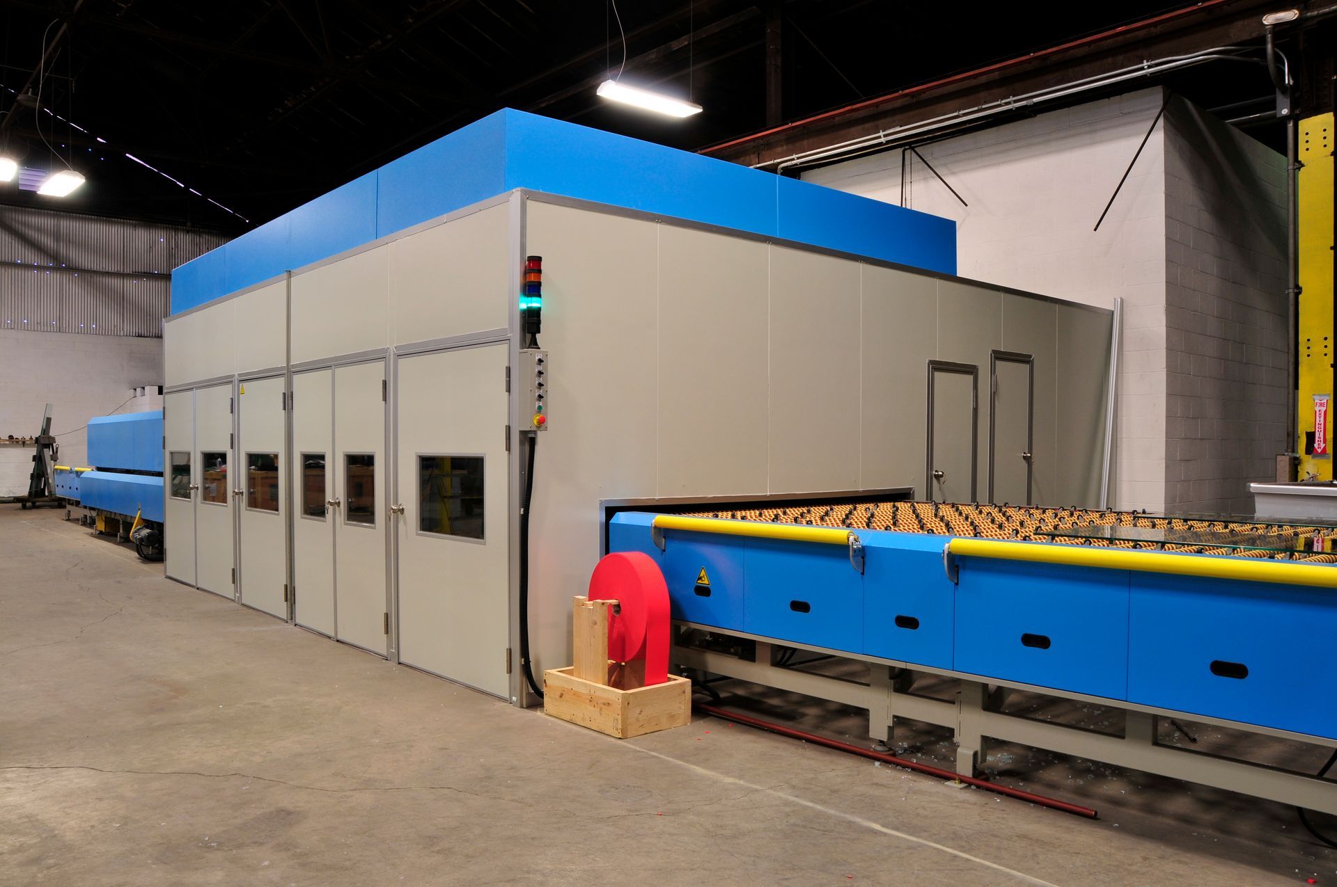 Large industrial oven with blue and gray panels, processing glass sheets in a factory setting.