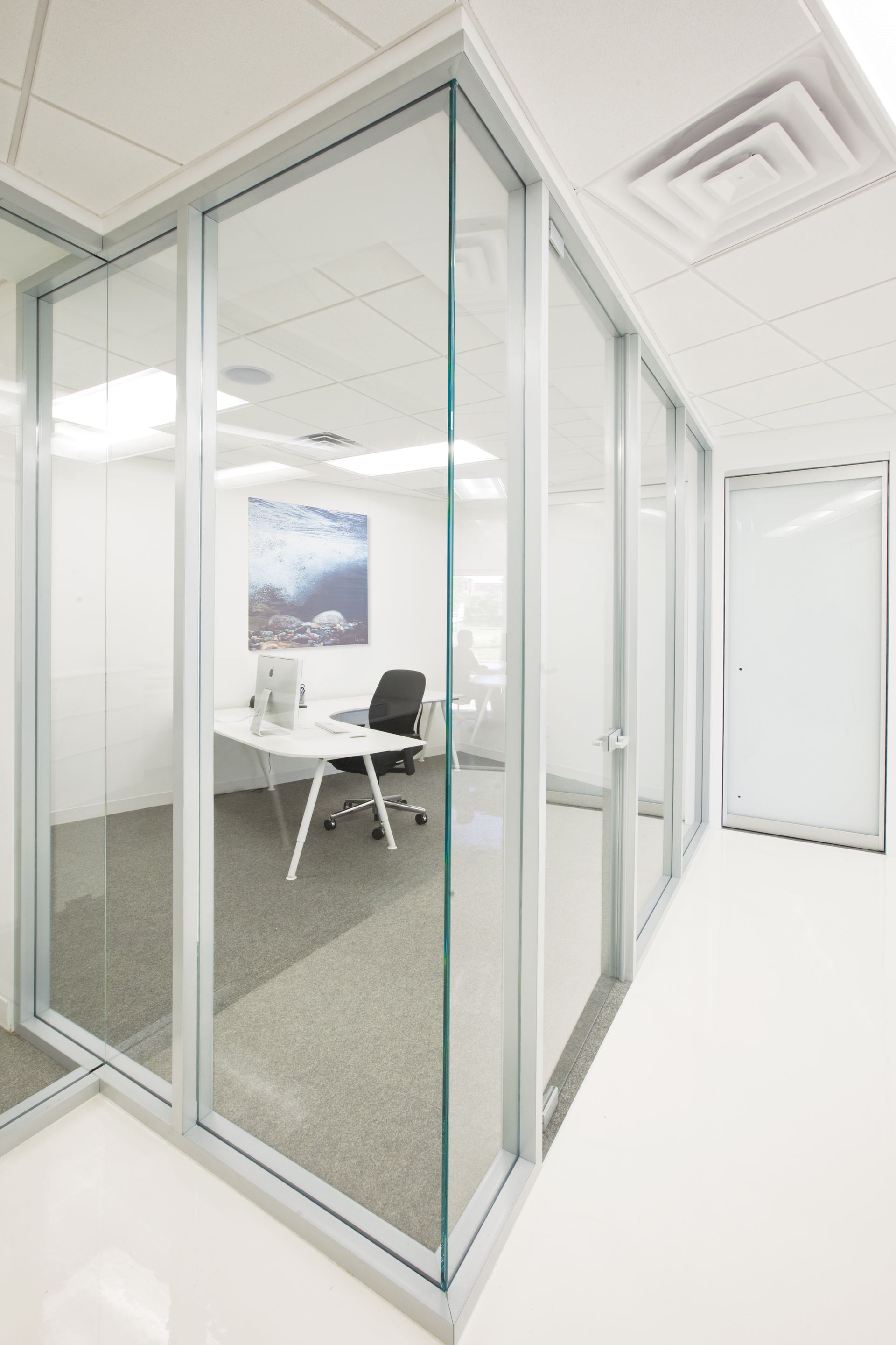 Office with glass walls; white desk, chair, and artwork visible inside.