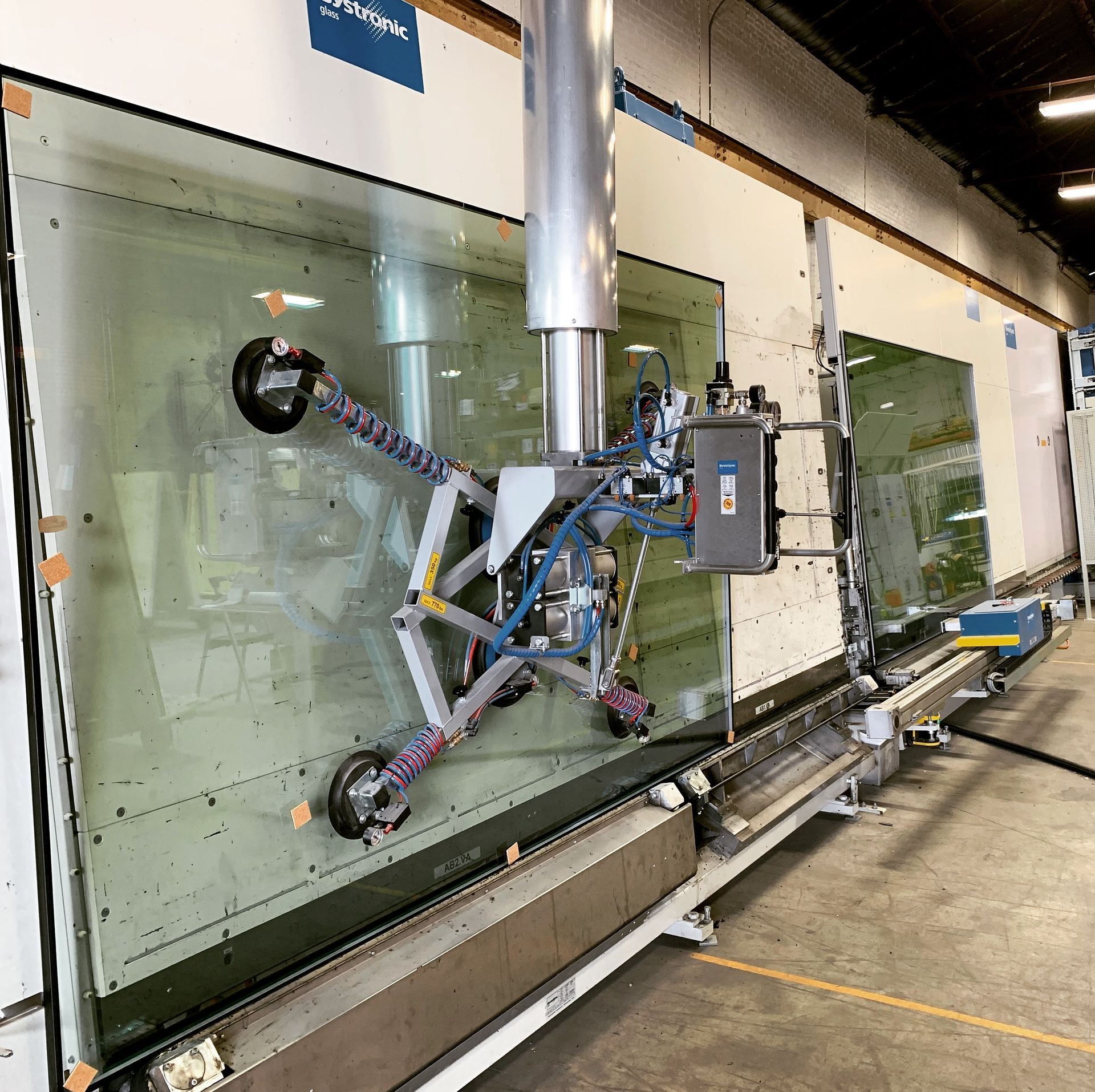 Glass panel being held by a robotic arm inside a factory.