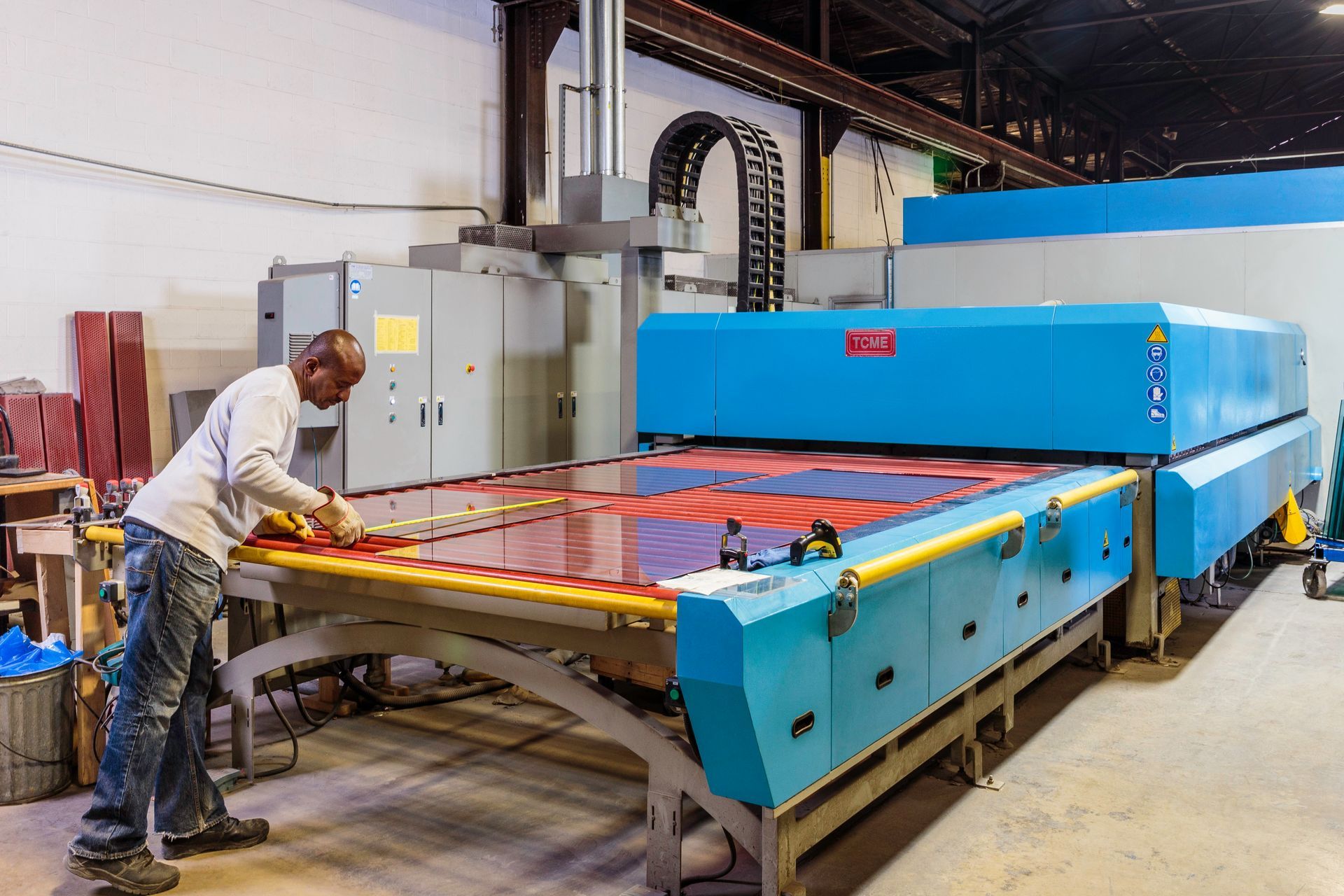 Man working with large glass cutting machine in factory.