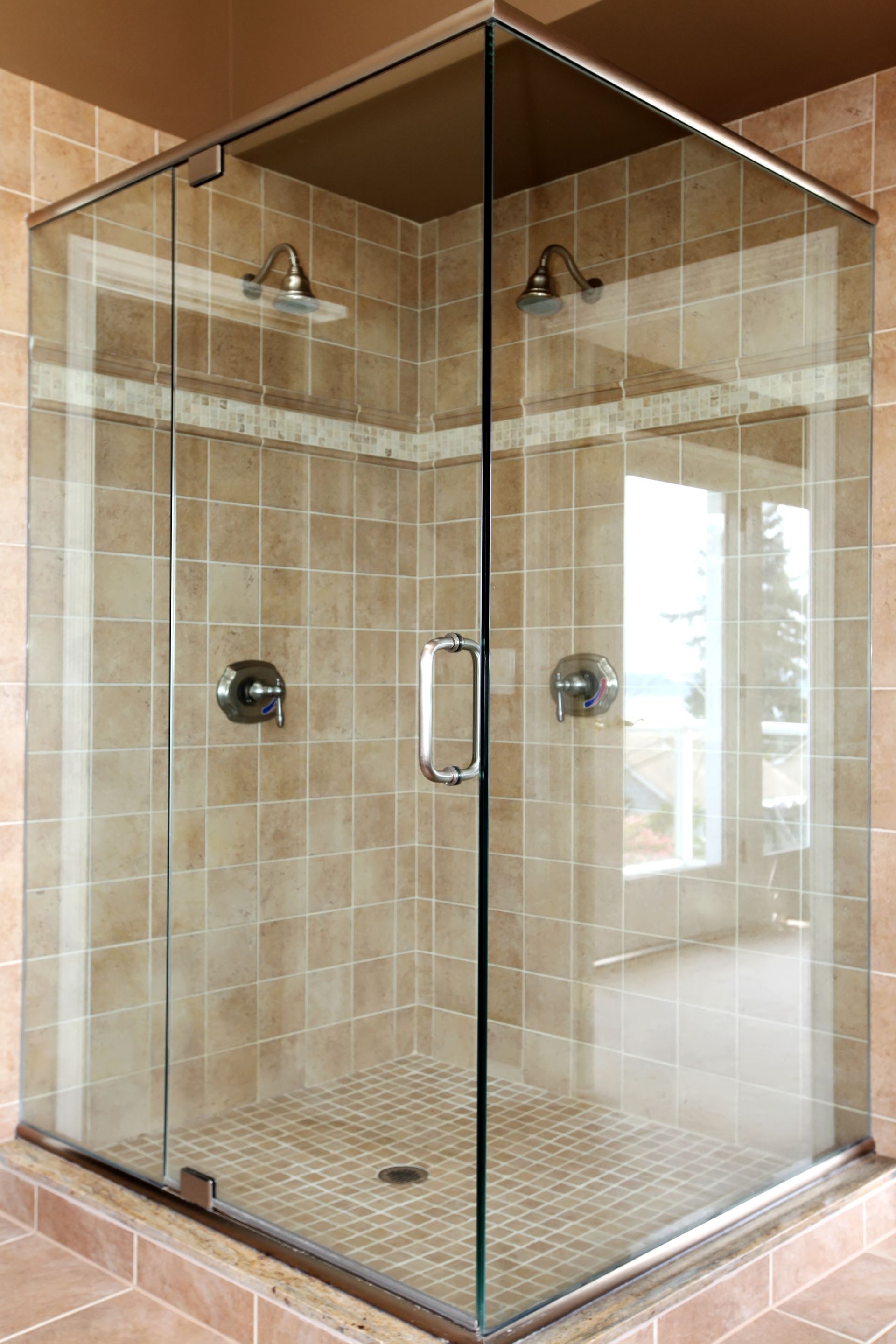 Glass shower enclosure with tiled walls, two shower heads, and chrome fixtures.