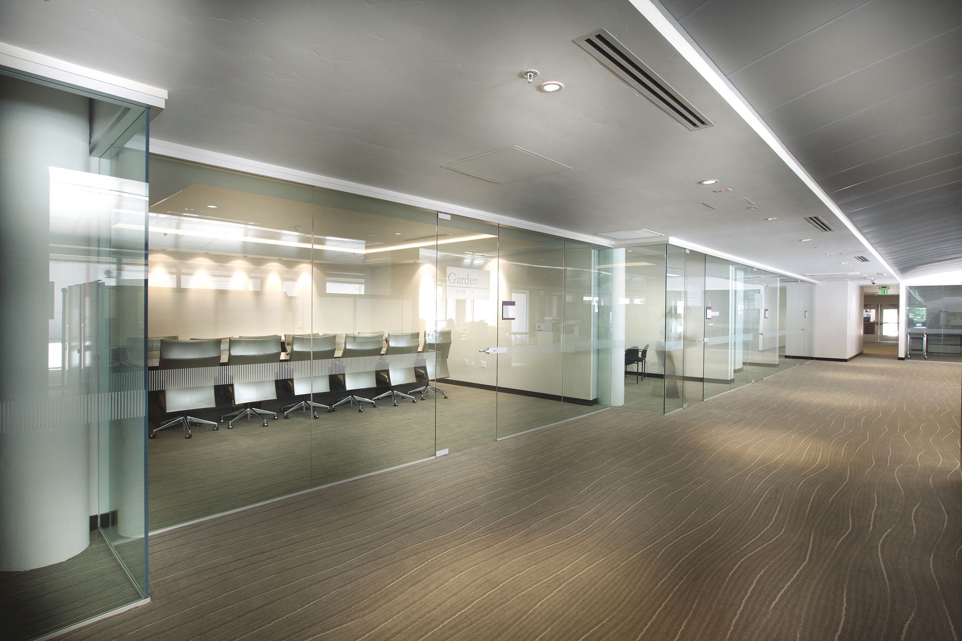 Modern office hallway with glass-walled conference rooms and carpeted floor.