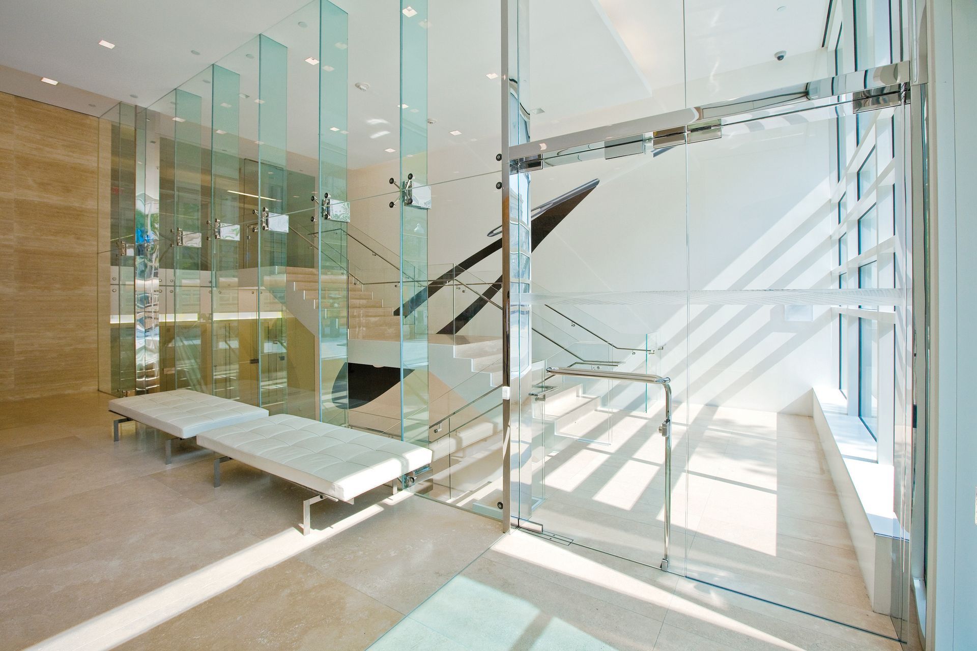Bright modern lobby with glass walls, a staircase, and benches, flooded with sunlight.