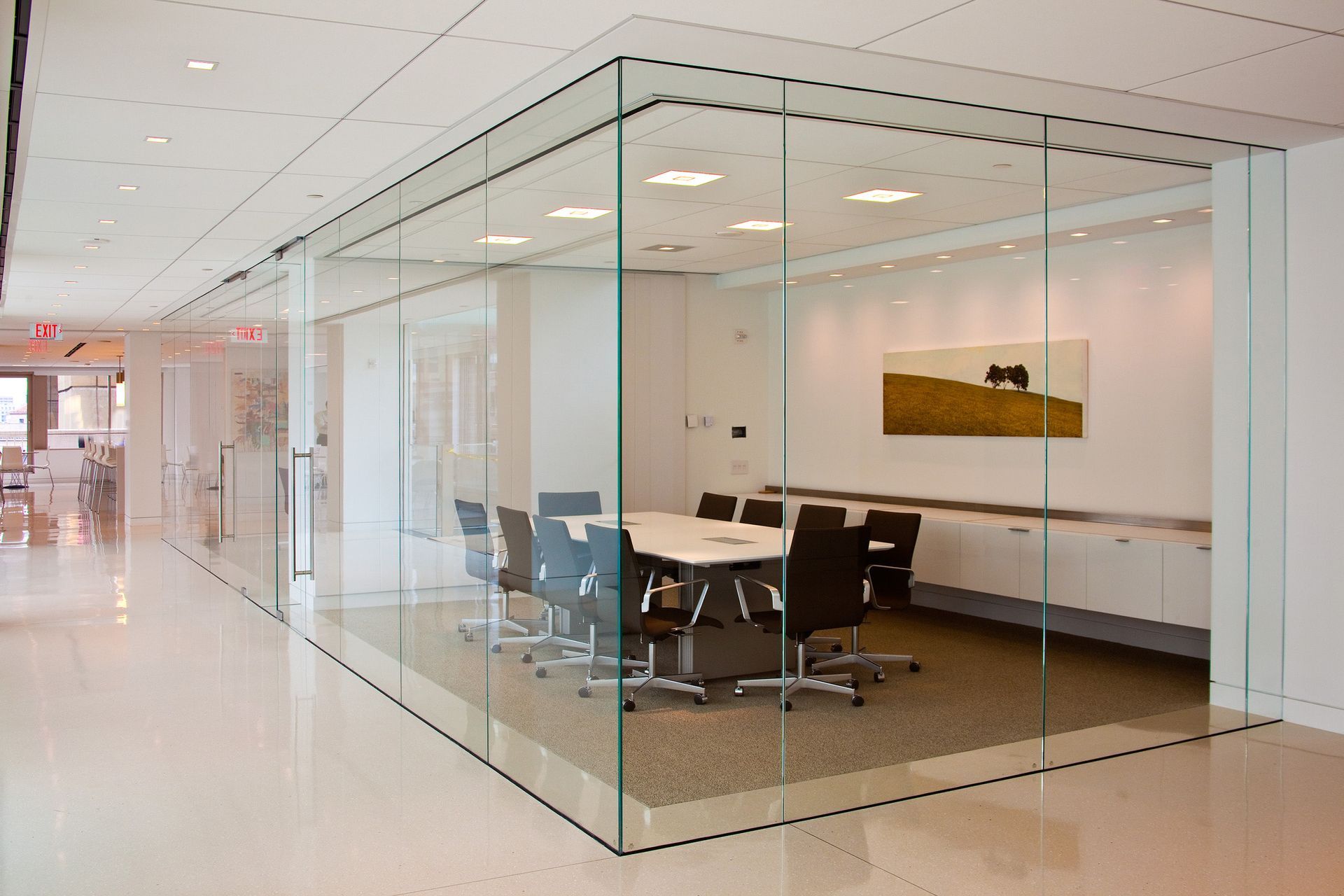Glass-walled conference room with a white table, black chairs, and beige carpet.