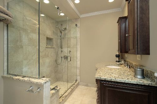 Bathroom with glass shower, dark vanity, granite countertop, and light-colored tile flooring.